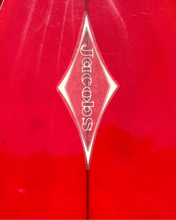 Load image into Gallery viewer, Red surface with a diamond-shaped 'Jacobs' logo in the center, against a green leafy background.