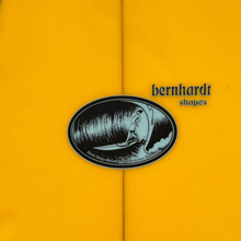 Load image into Gallery viewer, Close-up of a bright yellow surfboard with a black and white Bernhardt Shapes logo patch centered on the line, and partial blue edge visible at the top corners.