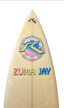 Load image into Gallery viewer, A close-up of a cream-colored surfboard with a colorful circular graphic and the words 'ZUMA JAY' in multicolored letters. 