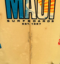Load image into Gallery viewer, Close-up of a cream-colored surfboard with a colorful 'MAUI SURFBOARDS EST. 1967' graphic on the top, showing the center seam and some handwritten markings.