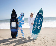 Load image into Gallery viewer, Two people holding Cirque du Soleil surfboards on a beach