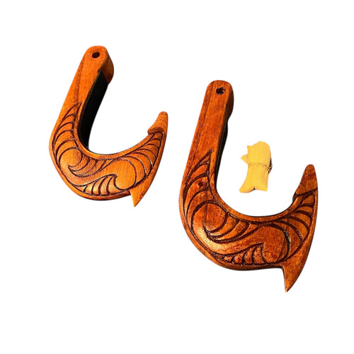 Two wooden fish hooks with intricate carvings on a white background