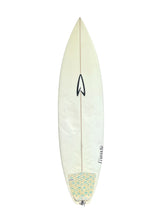 Load image into Gallery viewer, A vintage surfboard with a cream-colored fiberglass body, a black arrow logo, and a patterned yellow and blue tail patch, shown against a plain white background.