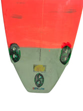 Load image into Gallery viewer, A close-up of a surfboard tail section, showing a bright coral-red upper portion and a muted sage-green lower portion with three black fin pads and small printed logos.